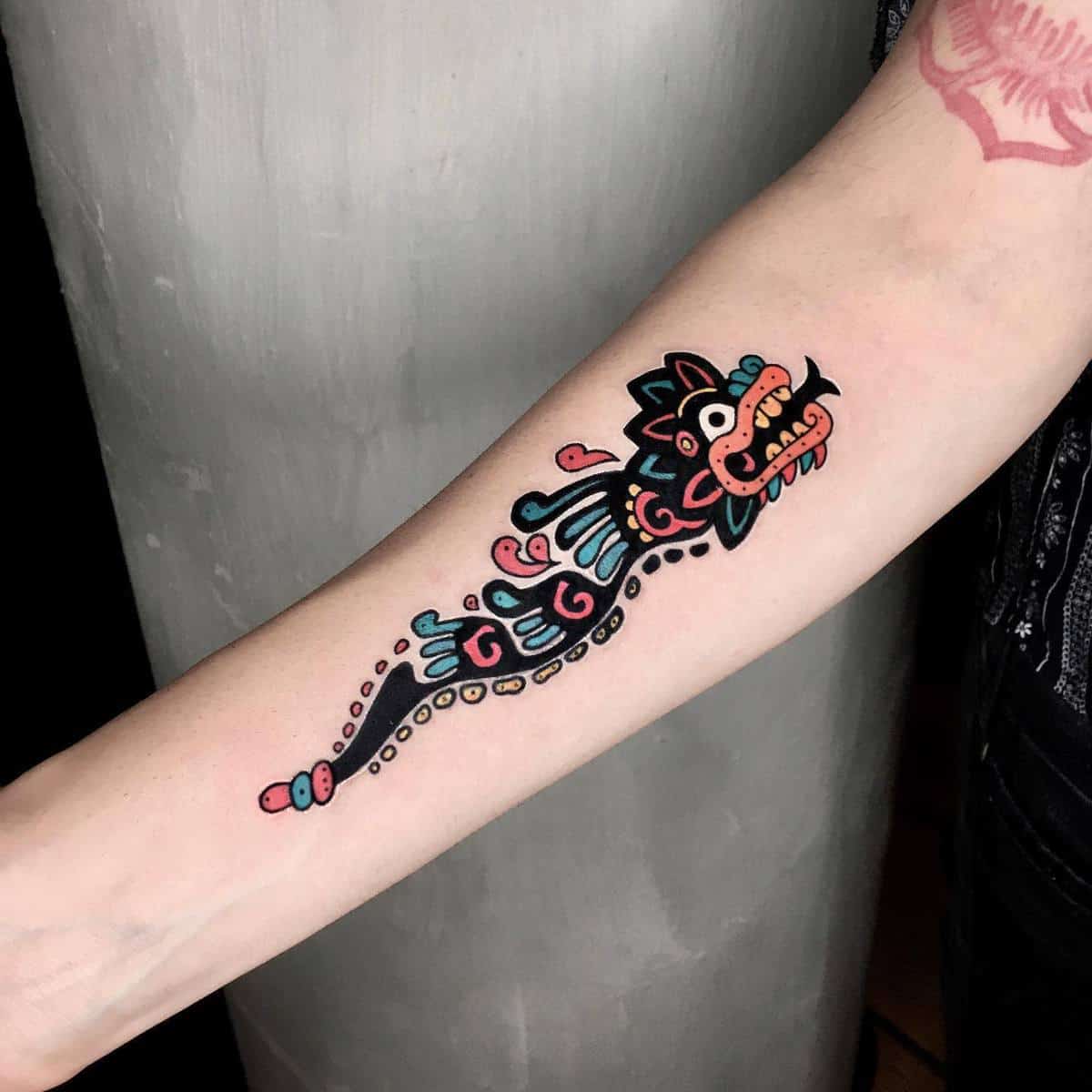 Stylized forearm tattoo of Quetzalcoatl with bold, vibrant tribal designs and colors