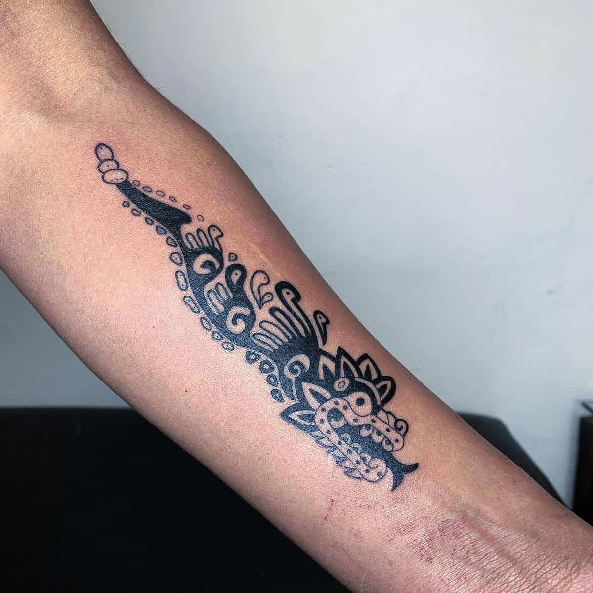 Black ink tribal-style forearm tattoo of Quetzalcoatl with flowing geometric patterns