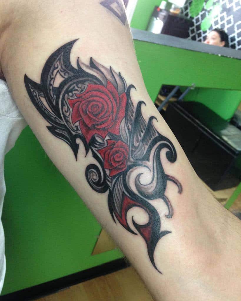 Tribal-style tattoo of red roses and abstract black swirls on an inner forearm