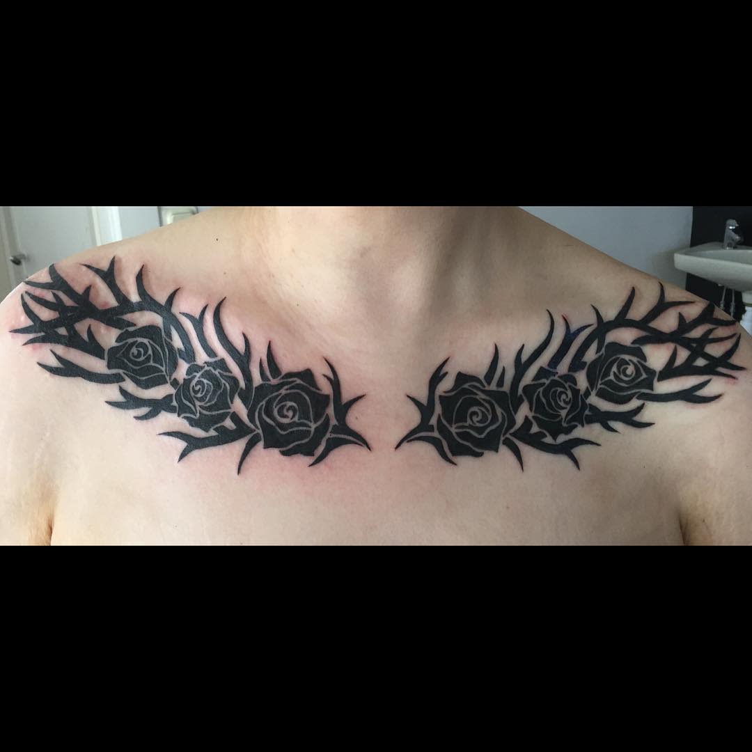 Tattoo of black roses with thorny vines across the collarbone area