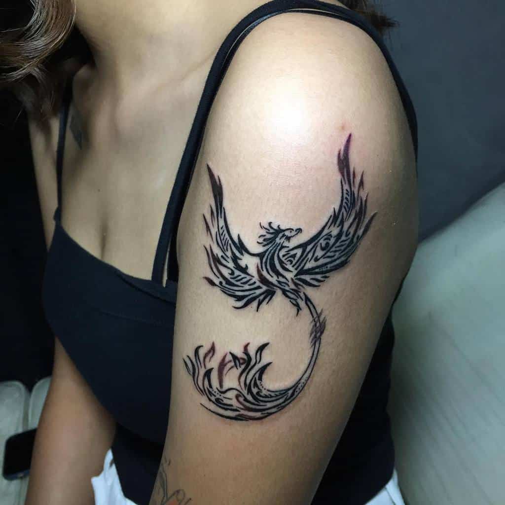 Tattoo of a stylized phoenix with tribal patterns on a woman's upper arm