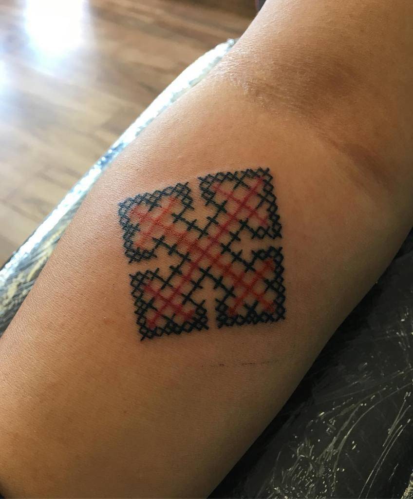 Cross-stitch tattoo of a geometric design with a plaid pattern in red and black, mimicking embroidered fabric
