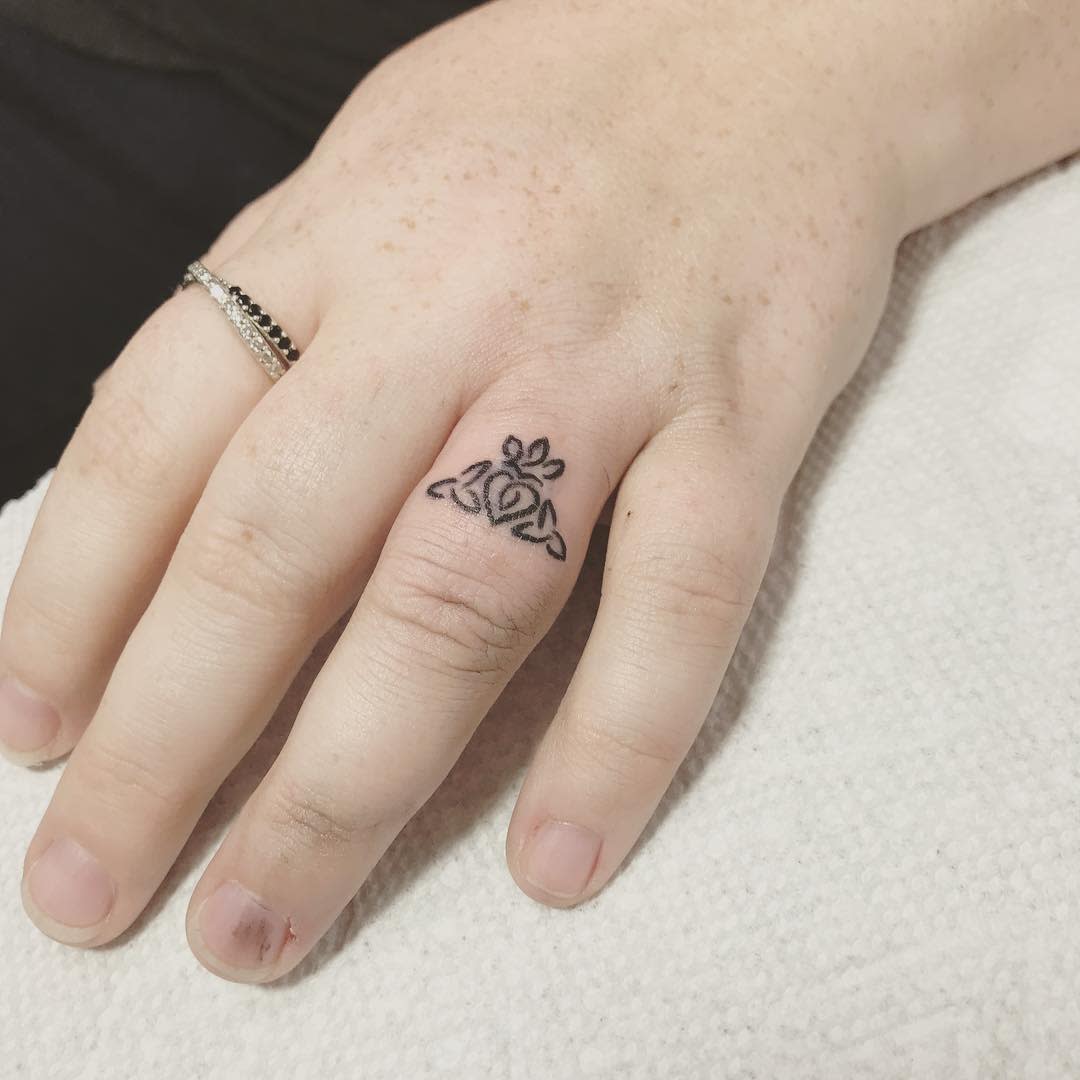 A small black crown ring tattoo shape like heart in the middle and leaves surrounding it