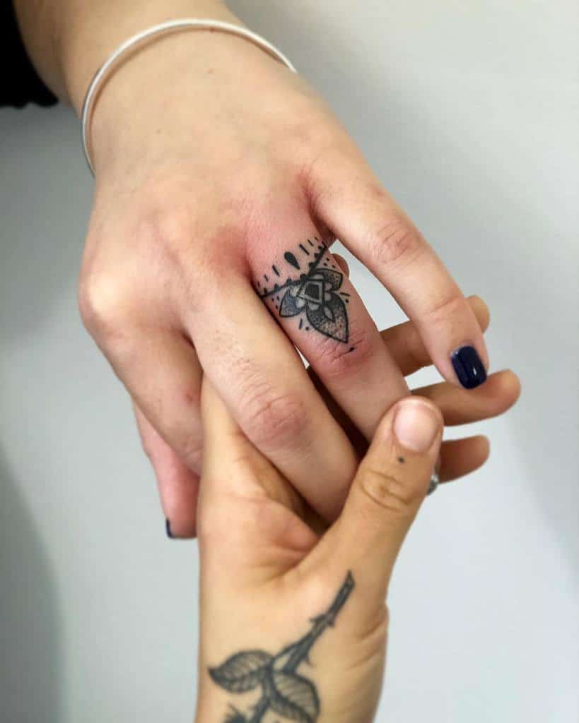 A black ink geometric flower ring tattoo with lines and droplet