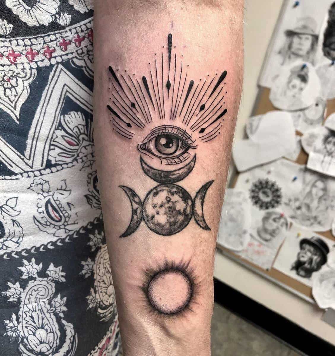 Forearm tattoo featuring an eye, crescent moons, a full moon, and a detailed geometric sun
