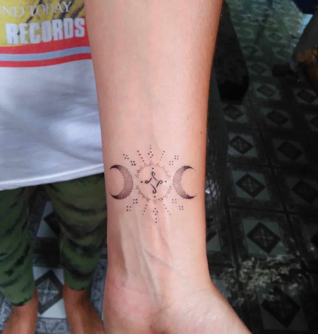 Wrist tattoo with a central symbol, crescent moons on each side, and dotted patterns