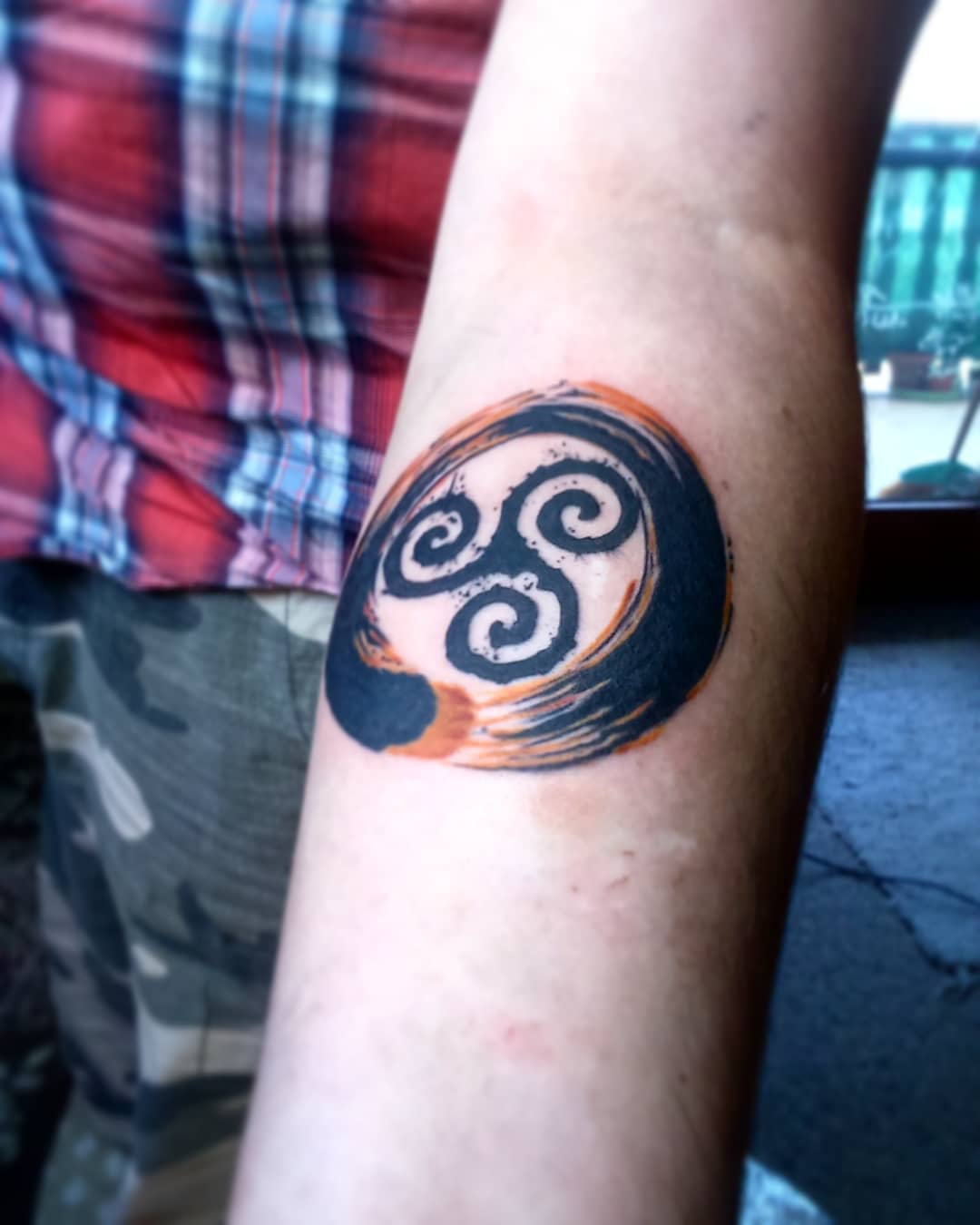 Forearm tattoo of a black and orange triskelion design