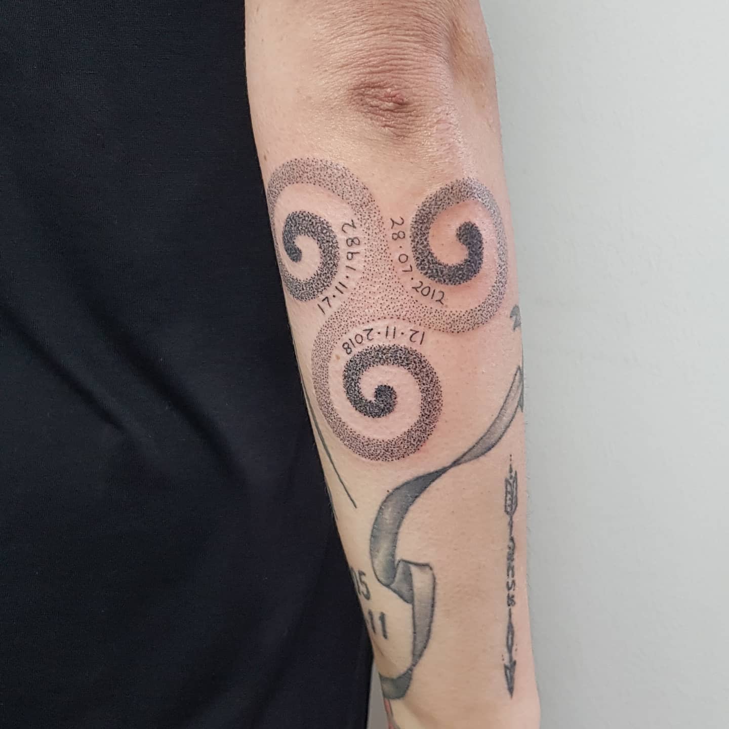 Forearm tattoo of a Triskelion with stippling effect, featuring dates, symbolizing significant life events and the continuity of time
