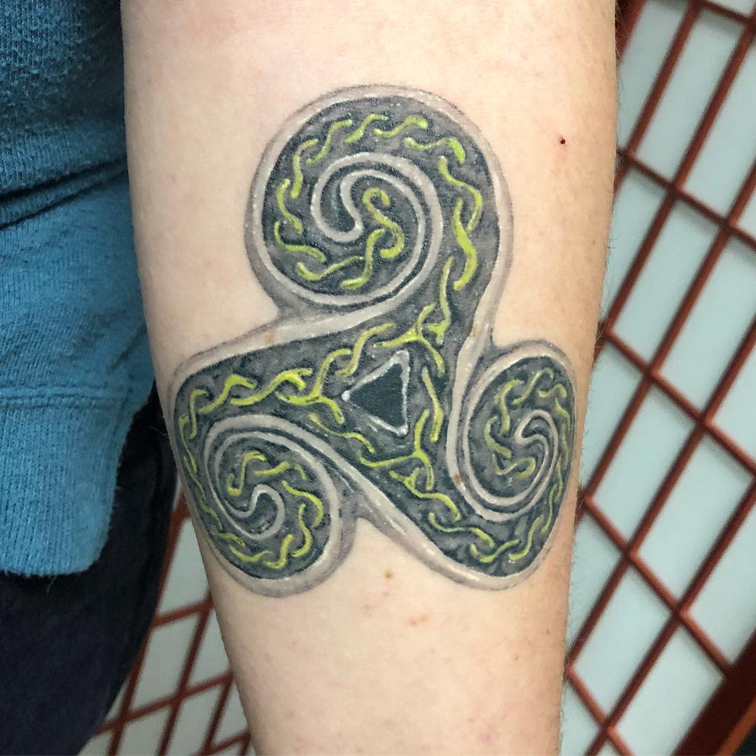 Tattoo of a Celtic triskelion with intricate green and yellow patterns on an arm