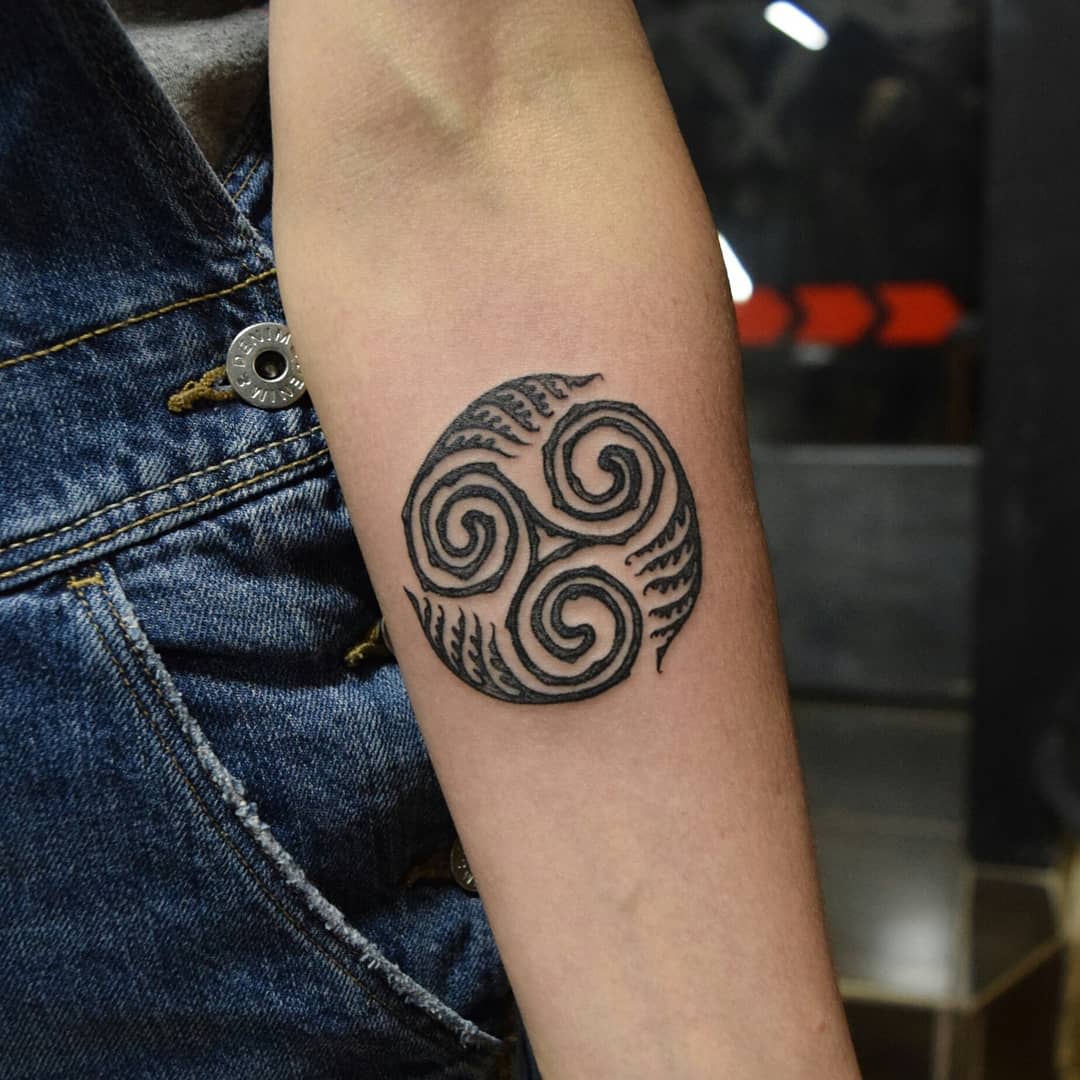 Forearm tattoo featuring a triskelion symbol with intricate patterns
