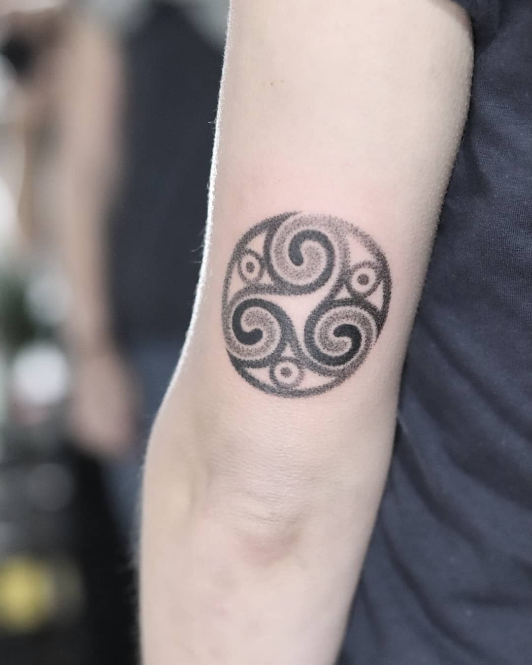 Arm tattoo of a circular Triskelion with a stippling effect, symbolizing balance and the flow of life