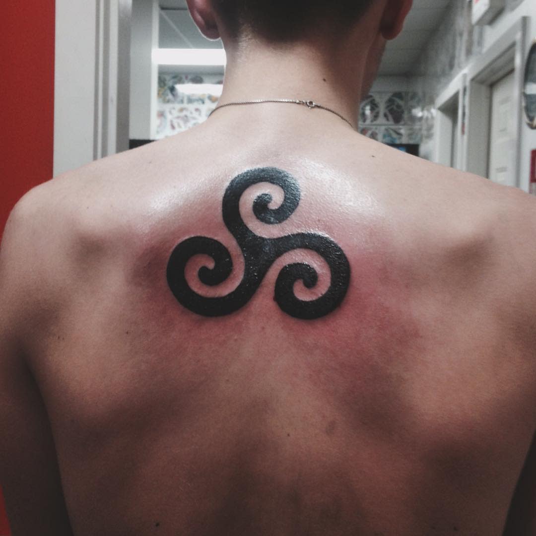Large black triskelion tattoo on the upper back