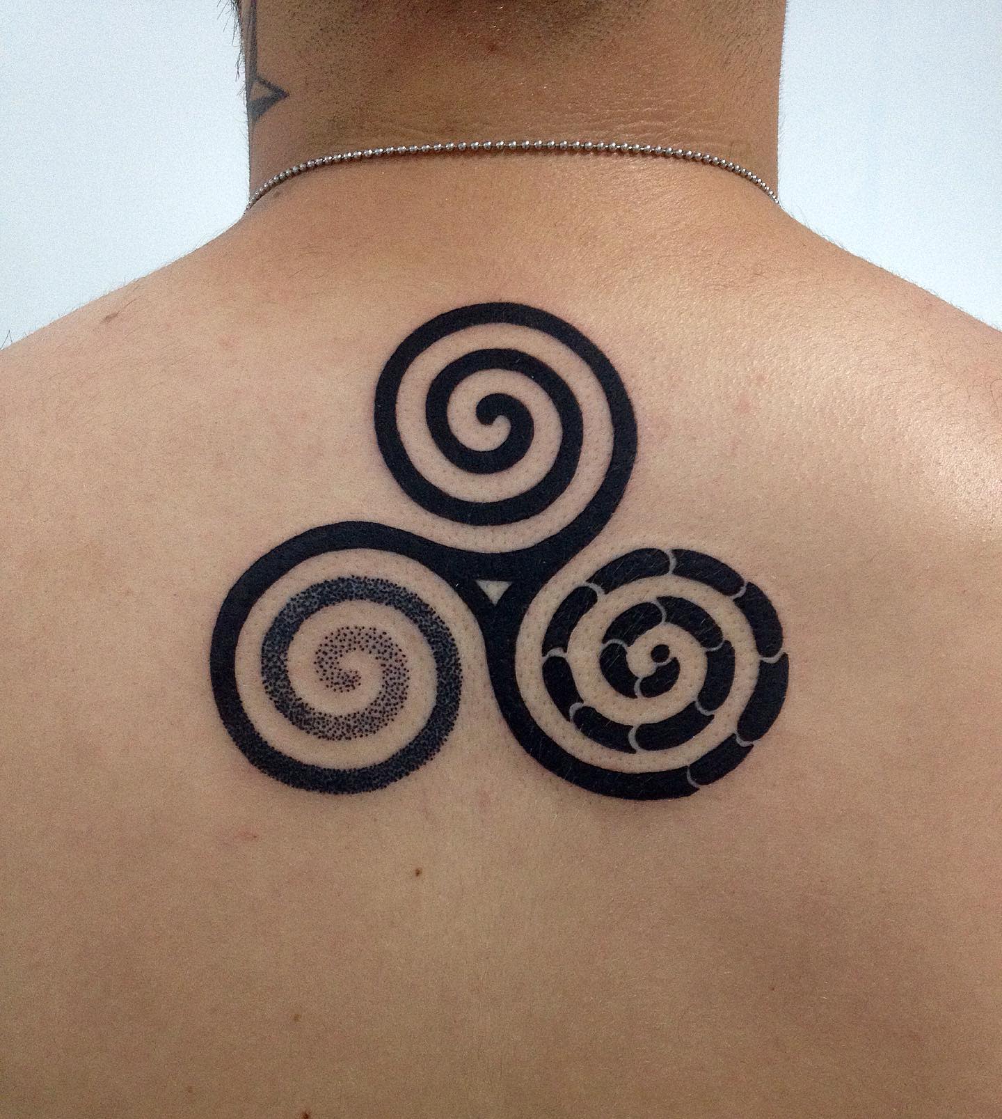 Back tattoo of a bold Triskelion with varied spiral patterns, symbolizing diversity in unity and life's cyclical nature
