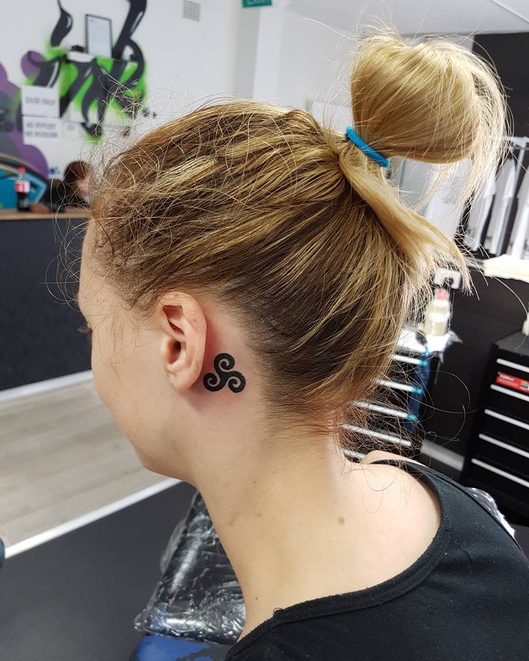 Behind-the-ear tattoo of a small, elegant Triskelion symbolizing balance and harmony