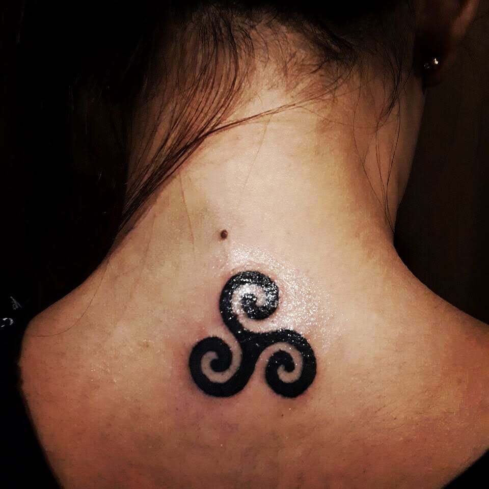 Tattoo of a black triskelion symbol on the back of neck