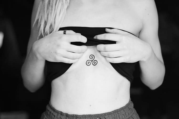 Sternum tattoo of a small Triskelion, representing inner balance and personal strength