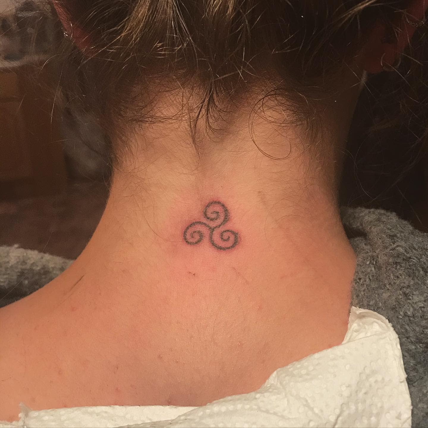 Small Triskelion tattoo on the back of the neck, symbolizing unity, balance, and personal growth