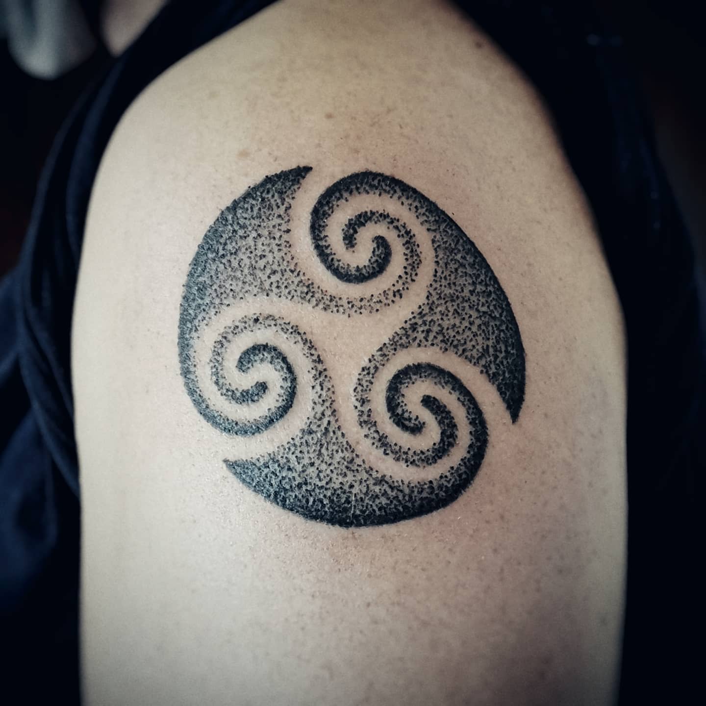 Arm tattoo of a bold, stippled Triskelion, symbolizing dynamic movement and continuity