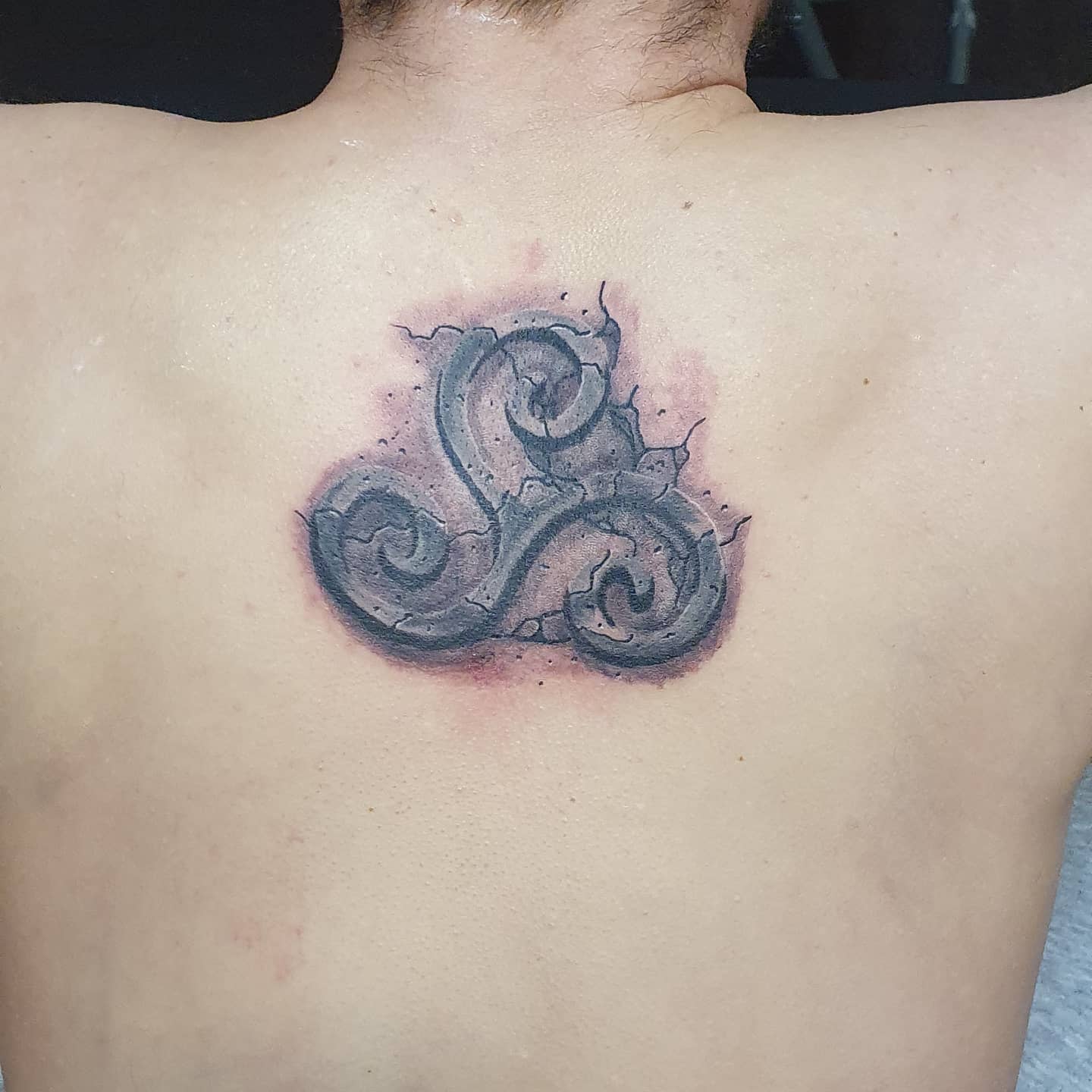 Back tattoo of a textured Triskelion with watercolor effects, symbolizing resilience and transformation