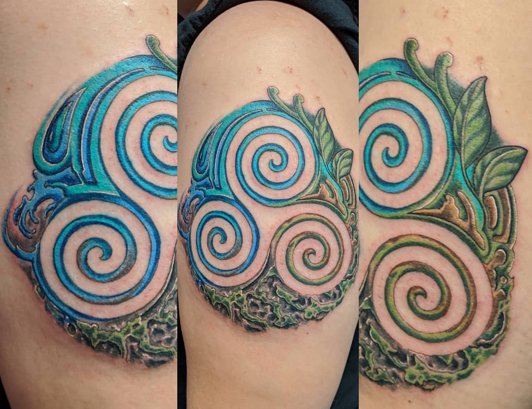 Vibrant arm tattoo of a Triskelion intertwined with nature elements, symbolizing life and renewal