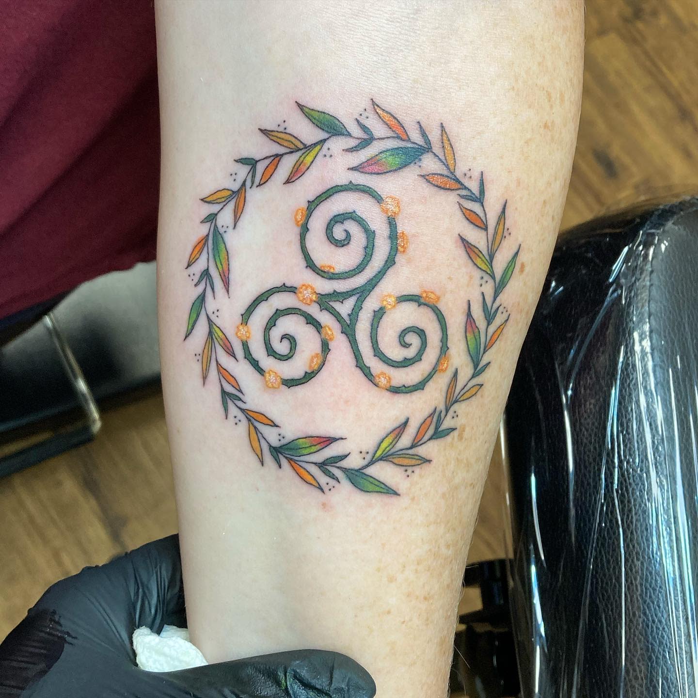 Delicate arm tattoo of a Triskelion encircled by a floral wreath, symbolizing growth and harmony