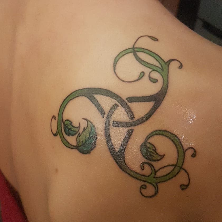 Shoulder tattoo of a Triskelion intertwined with green vines, symbolizing growth and natural cycles