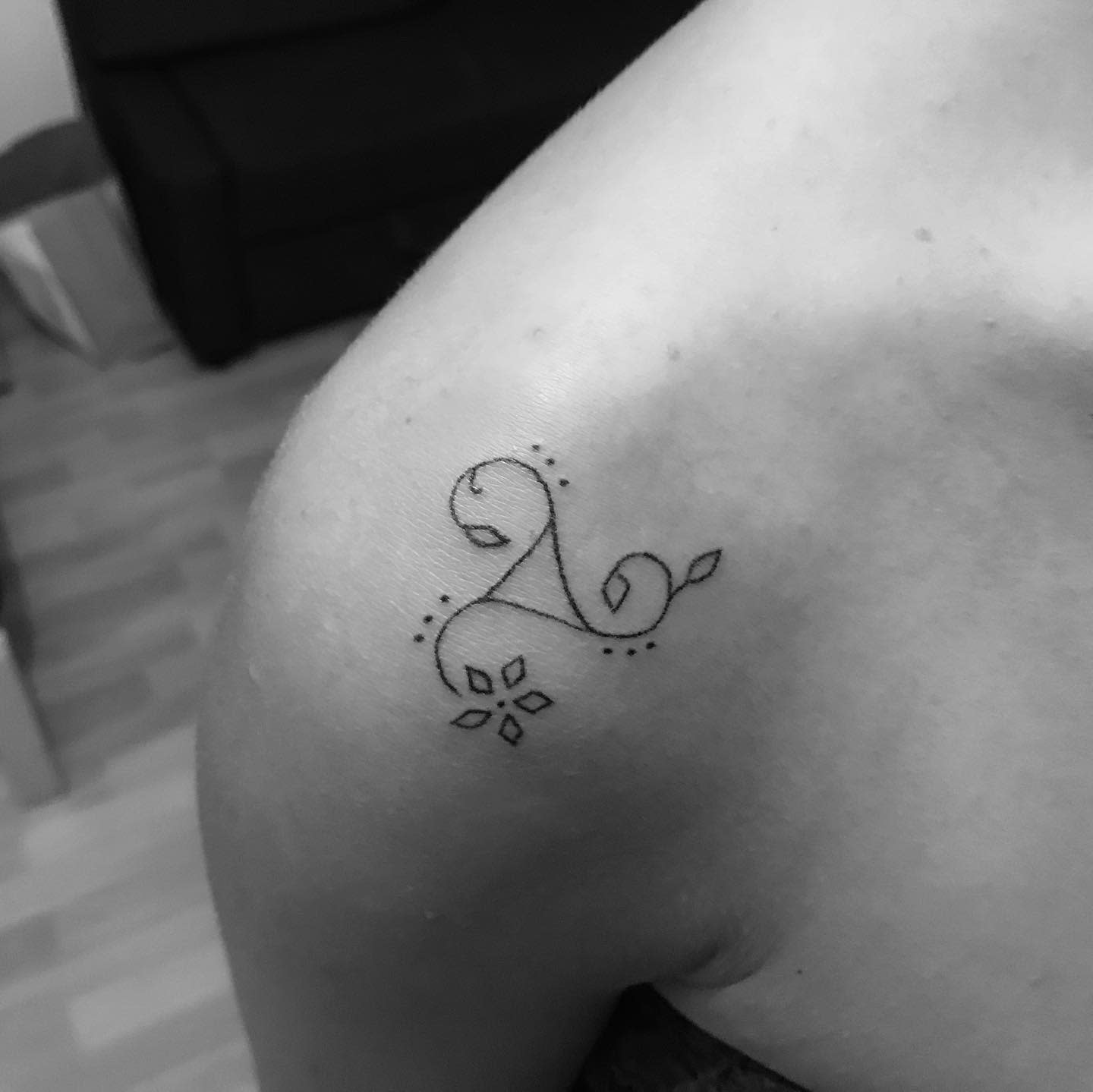 Delicate shoulder tattoo of a minimalist Triskelion with floral accents, symbolizing simplicity and growth