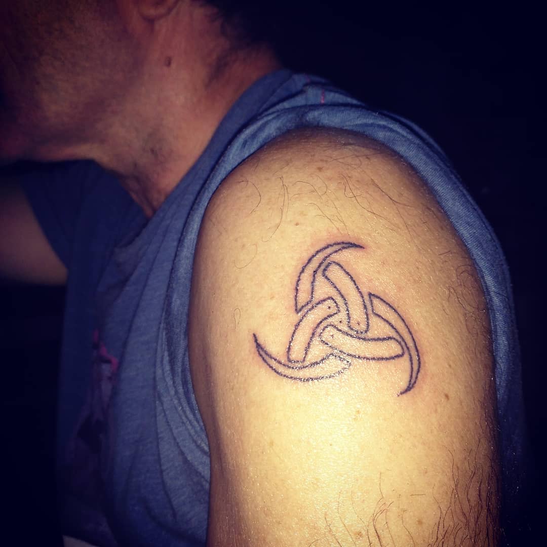 Upper arm tattoo of a simple, outlined Odin Triskelion, symbolizing motion, strength, and eternity