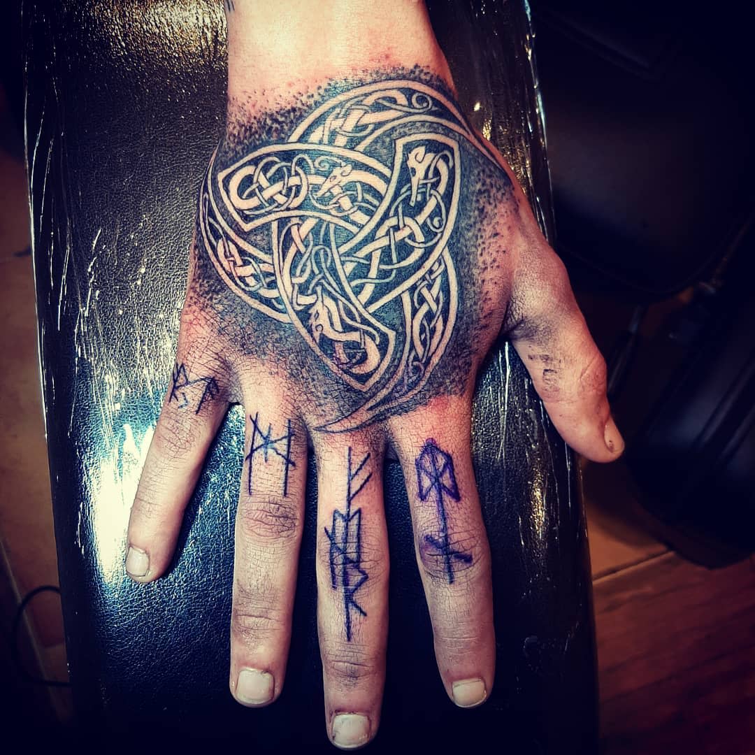 Intricate hand tattoo of a Celtic Triskelion surrounded by runes, symbolizing ancient power and protection