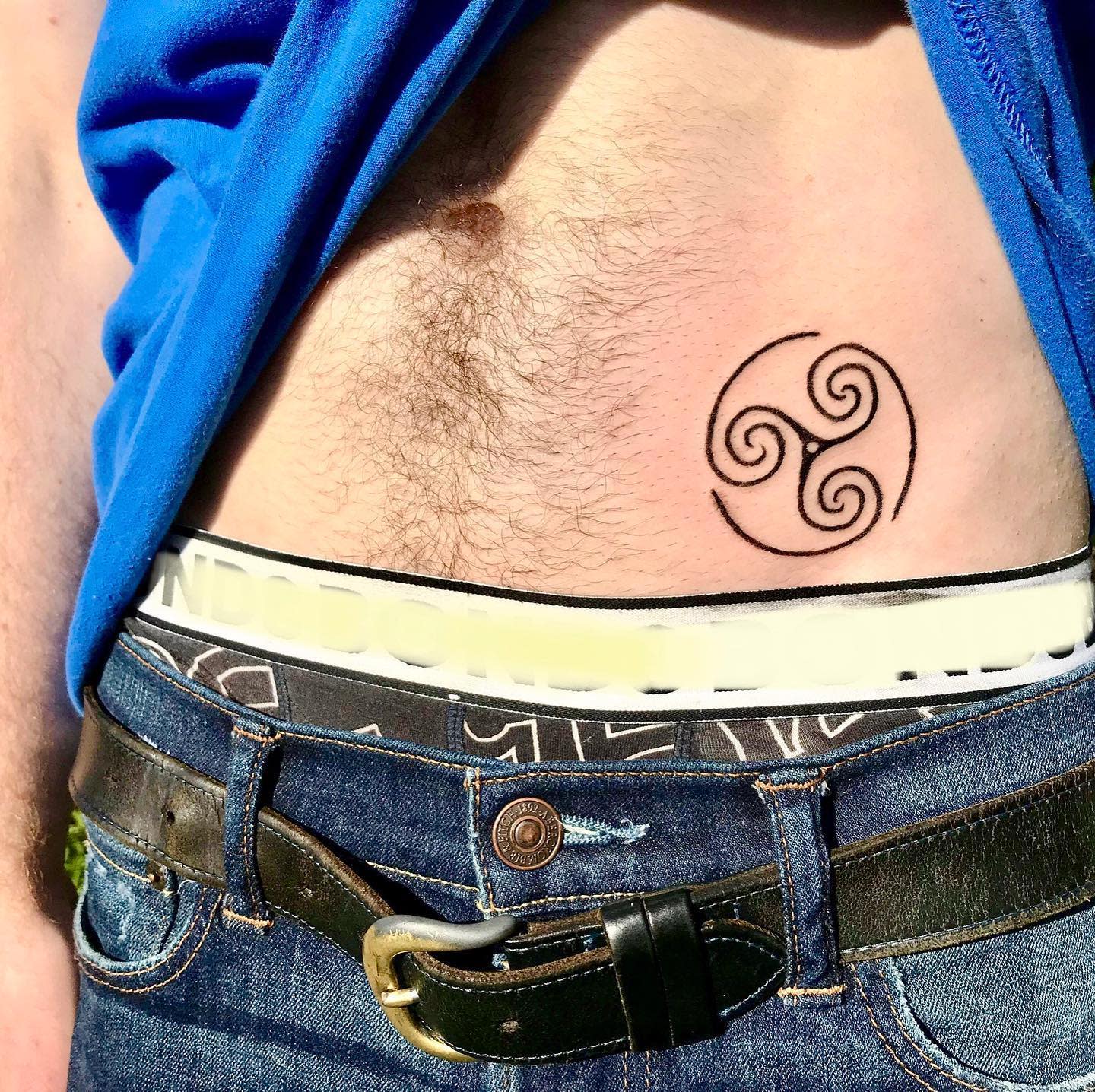 Tattoo of a triskelion symbol on lower stomach