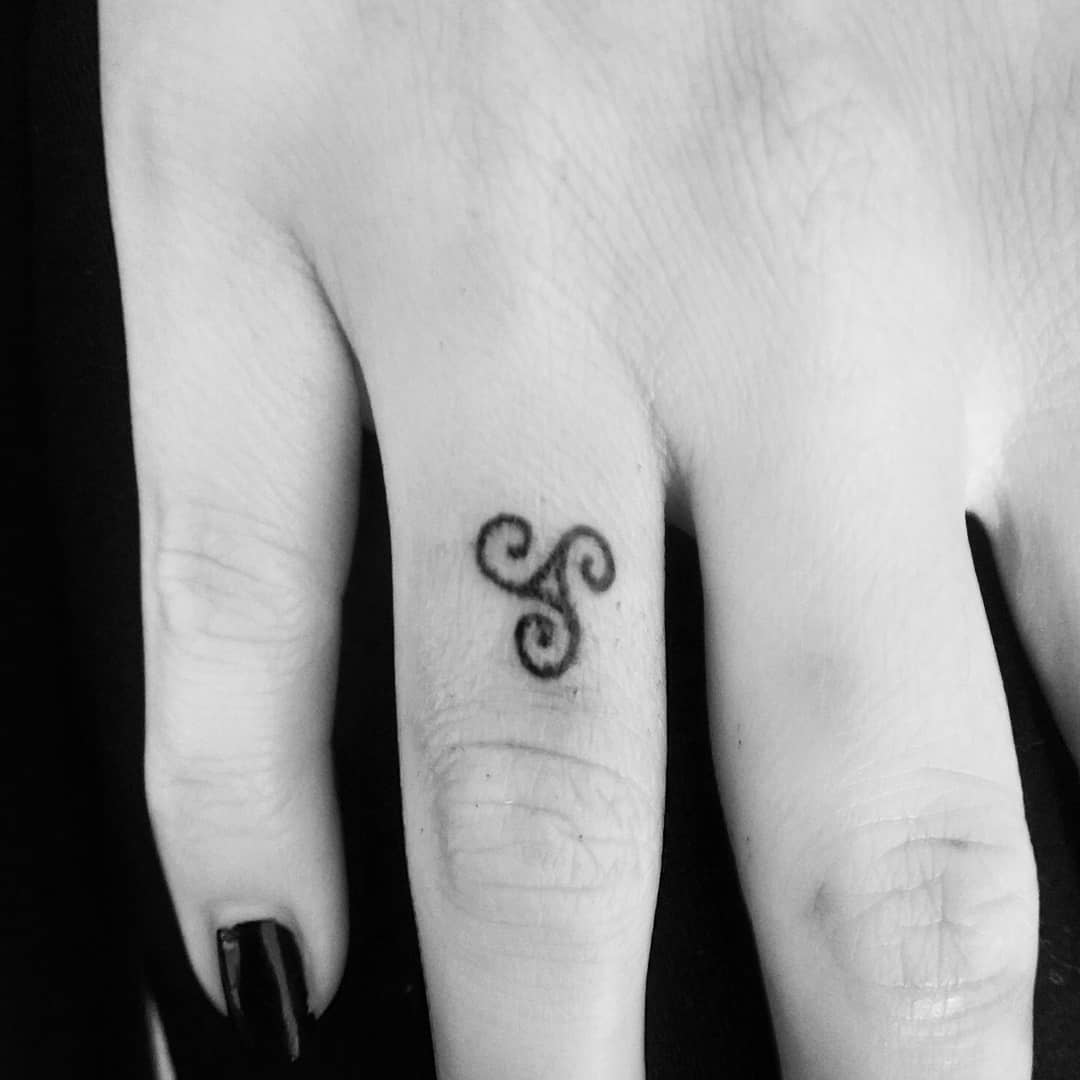 Small triskelion tattoo located between the thumb and index finger