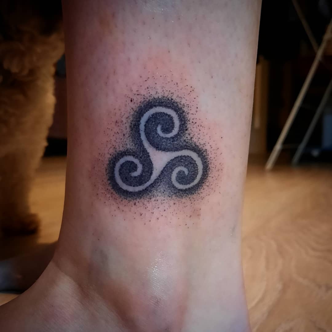 Ankle tattoo of a Triskelion with stippling effect, symbolizing balance and dynamic energy