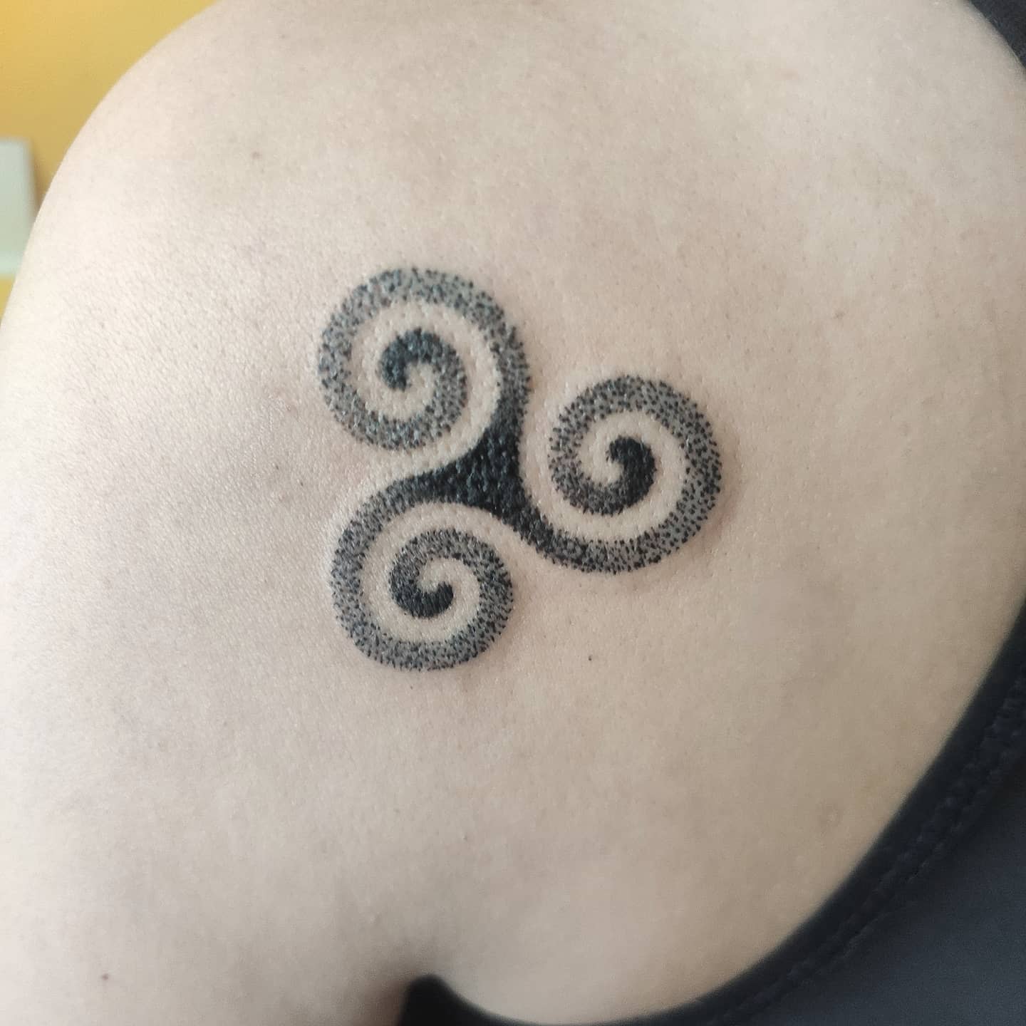 Small black triskelion tattoo with intricate dots on a shoulder