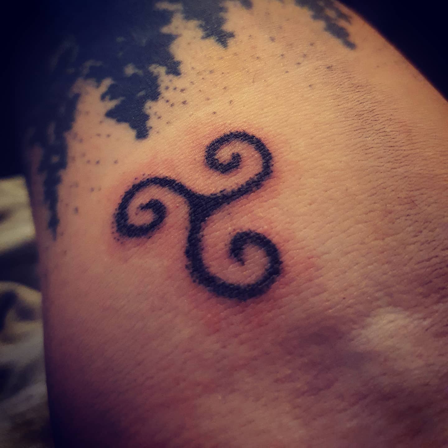 A small tattoo of a black triskelion symbol on skin