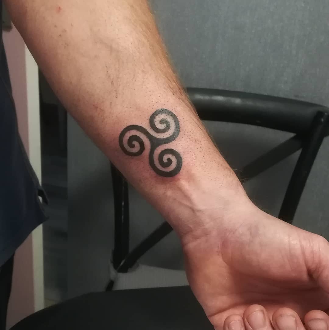 Wrist tattoo featuring a black triskelion symbol with three interlocking spirals