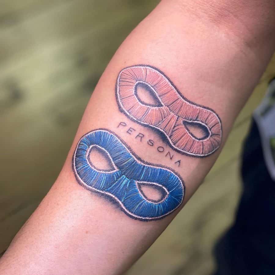 Tattoo featuring two stitched masks with thread-like textures, symbolizing duality and identity, with 'PERSONA' written below.