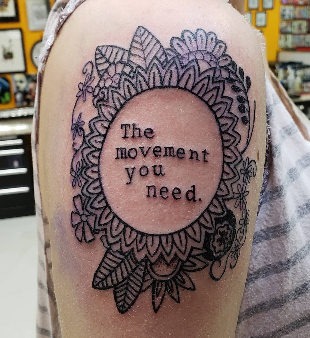 Upper arm tattoo of flowers and leaves with text "The movement you need" in the center