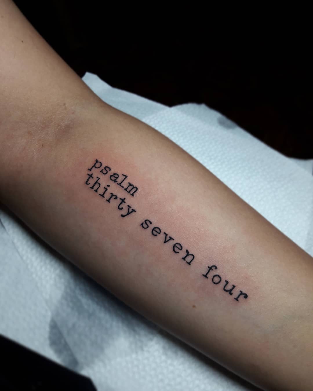 Forearm tattoo reads "psalm thirty seven four" in black typewriter-like font