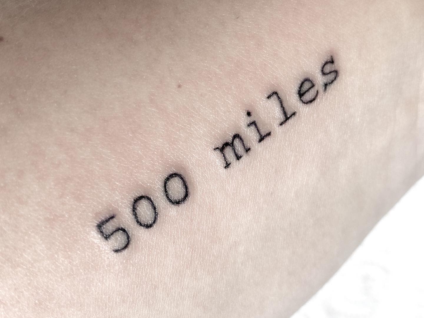 Tattoo on skin with the text "500 miles" in typewriter font
