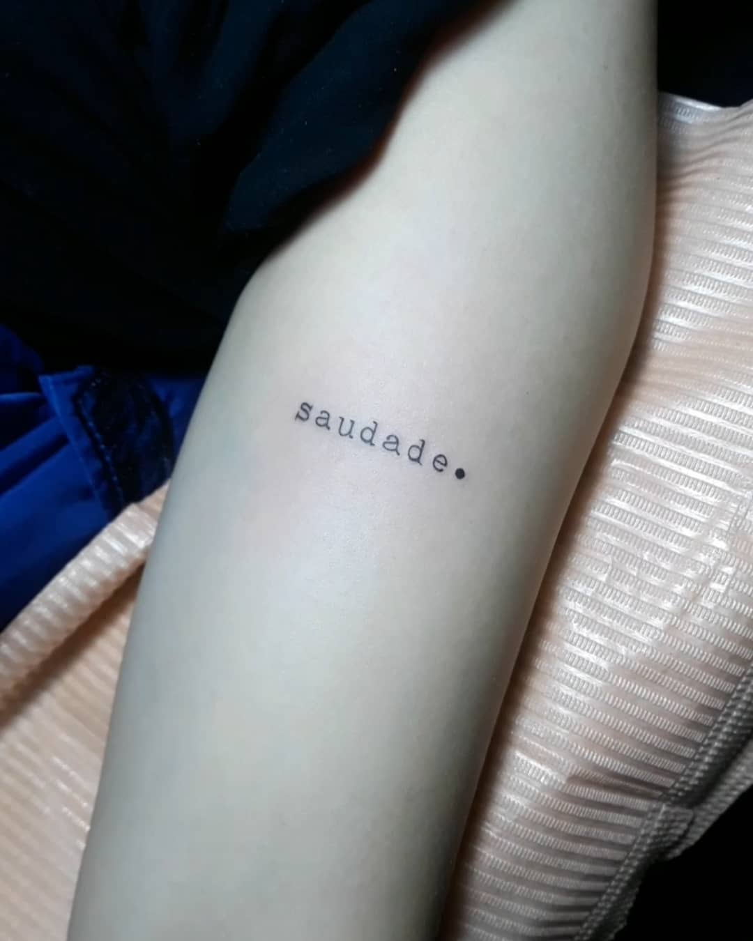 Tattoo on an arm with the word "saudade" in black ink