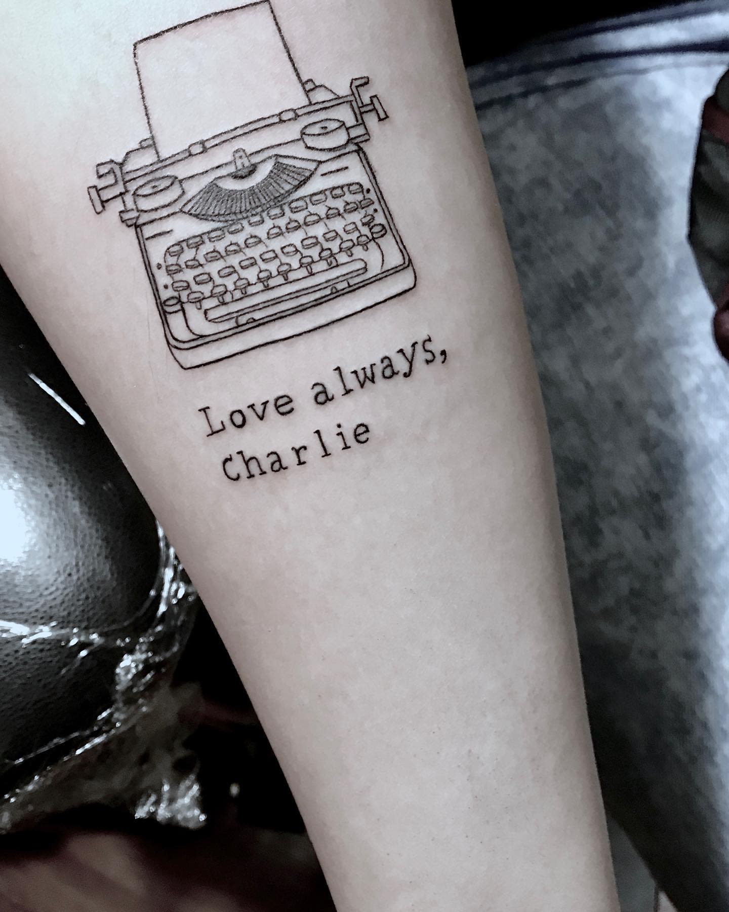 Tattoo of a typewriter with the text "Love always, Charlie" on a forearm
