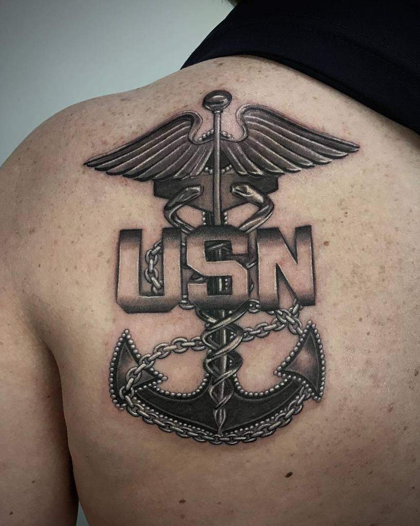 Tattoo featuring a caduceus, navy anchor, and chain with "USN" on person's back
