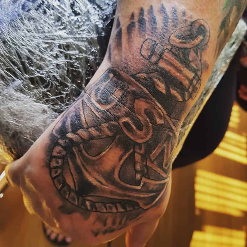 Tattoo of an anchor with "USN" wrapped in rope on a person's forearm, symbolizing their navy service