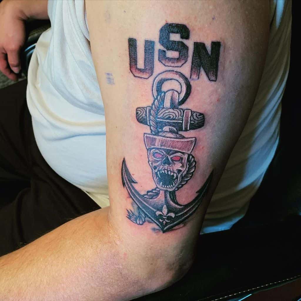 A muscular arm with a tattoo of "USN" above an anchor, skull, and navy design
