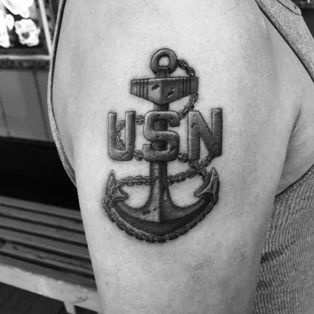 Black and white tattoo of an anchor and chain with "USN" inked on a person's upper arm, showcasing navy pride