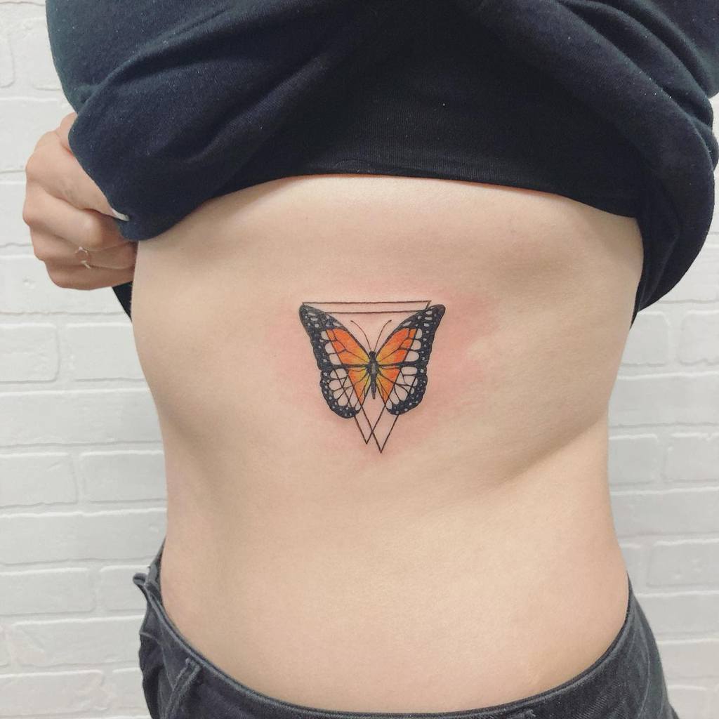 A person shows a butterfly tattoo on their side, featuring geometric black lines and an orange center