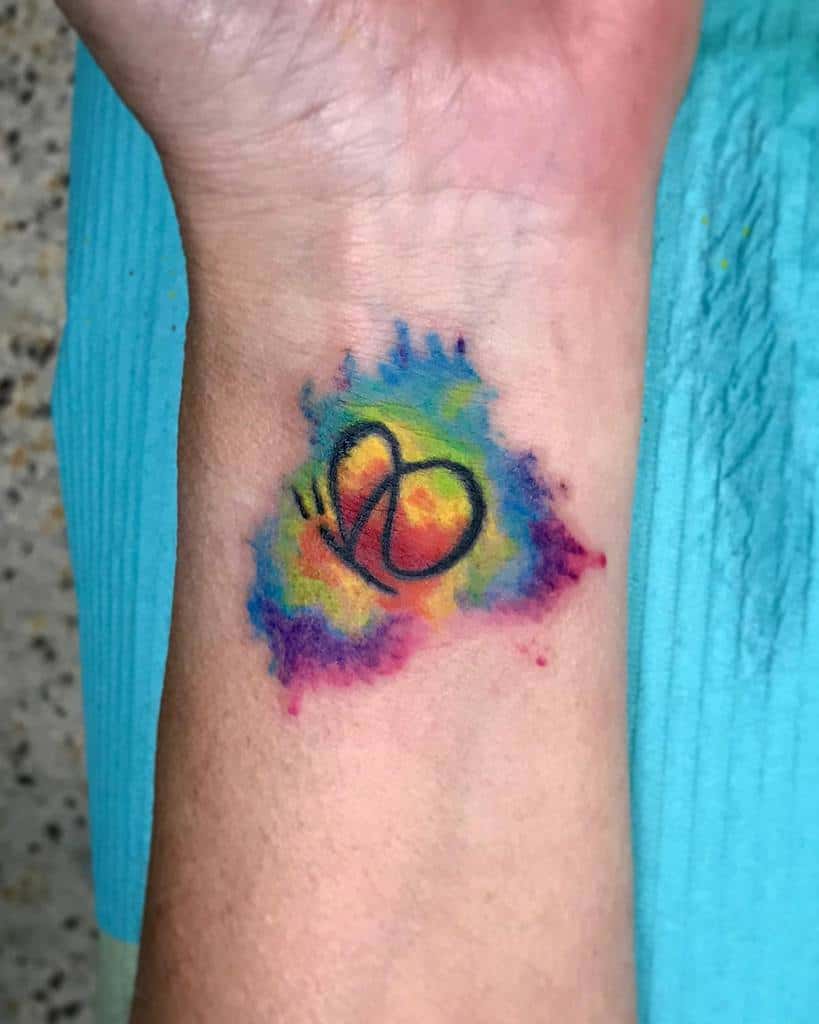 Tattoo of a butterfly wing on a wrist, surrounded by a colorful watercolor splash