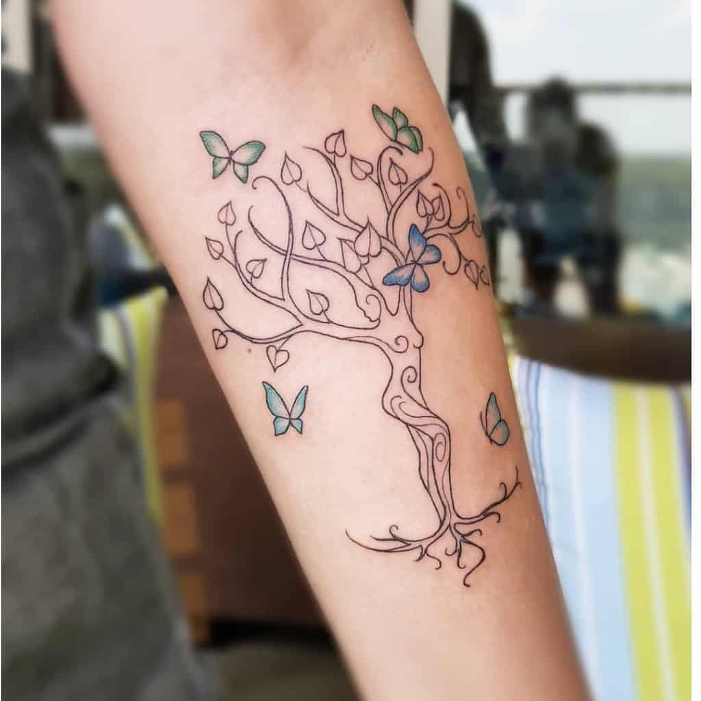 Forearm tattoo of a minimalist tree with green-blue butterflies around it