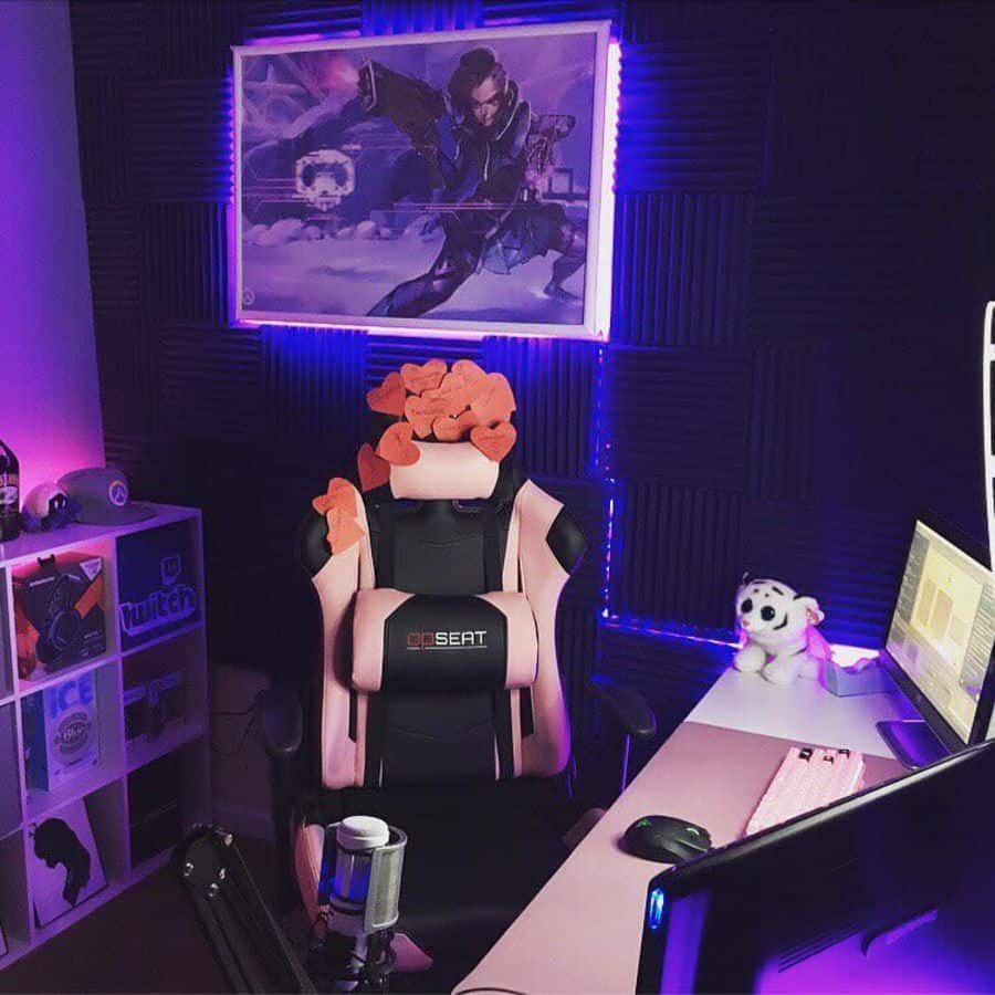 Gaming setup with pink chair, purple LED lights, and computer monitors, a poster and plush toys decorate the room