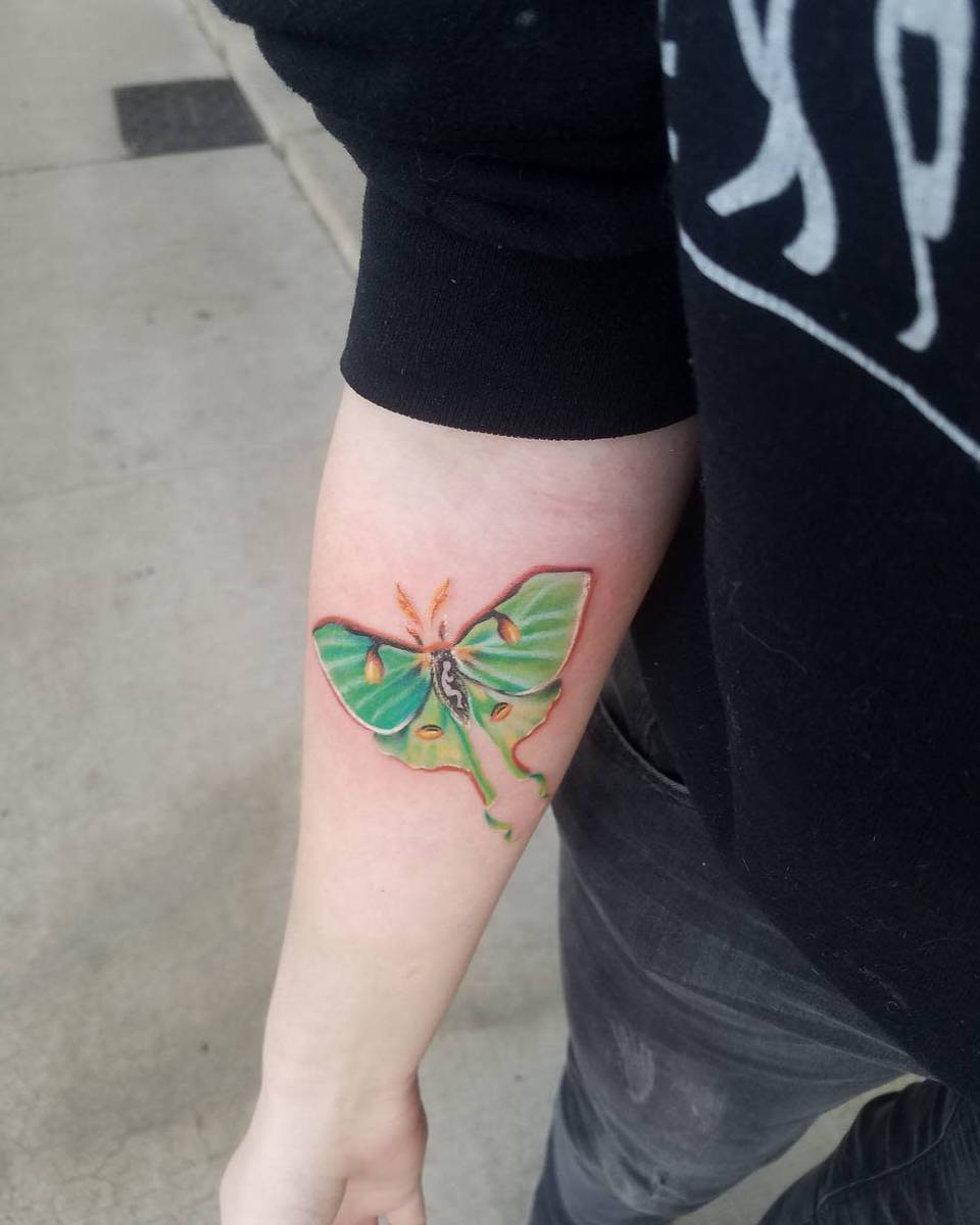 A large, colorful moth tattoo on an inner forearm, showcasing vibrant green wings and intricate details